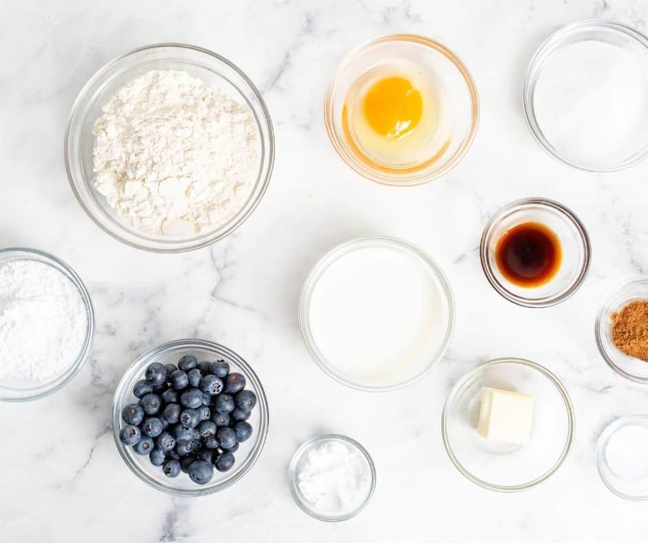 : A collection of essential baking ingredients for blueberry donuts: all-purpose flour, granulated sugar, and baking powder, arranged on a white surface.