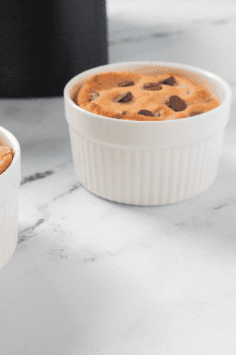 Air fryer chocolate chip cookie in a cup topped with melted chocolate chips and served warm in a ramekin.