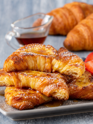 Air fryer croissant french toast topped with roasted strawberries and powdered sugar on a white plate