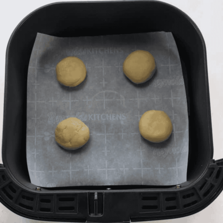 A hand pressing a large white marshmallow into the center of a warm, round sugar cookie to create the snowman's head.