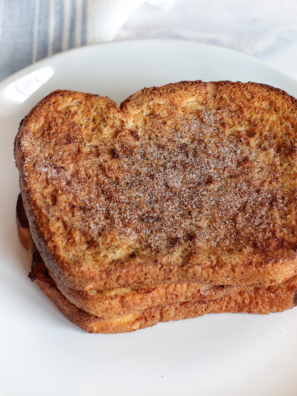 Golden air fryer pumpkin French toast slices on a white plate, dusted with powdered sugar and drizzled with maple syrup
