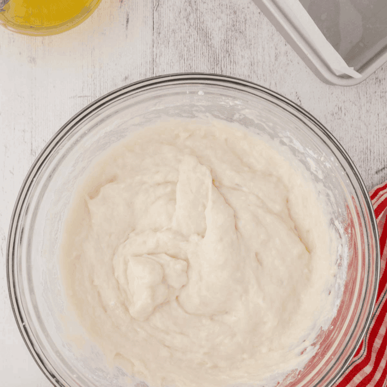 A whisk mixing dark molasses, melted butter, and brown sugar in a large bowl until the texture is smooth and glossy.
