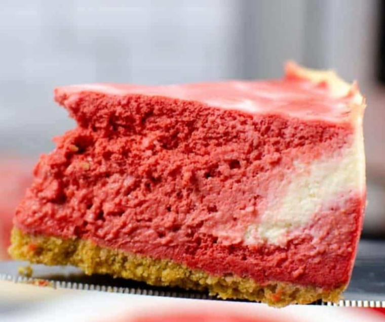 Slice of Instant Pot Christmas Swirl Cheesecake showing the red velvet swirl, served with whipped cream and mint.
