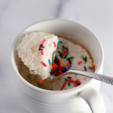 Air fryer vanilla mug cake with icing drizzled over the top and rainbow sprinkles in a white mug