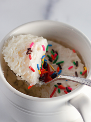 Air fryer vanilla mug cake with icing drizzled over the top and rainbow sprinkles in a white mug