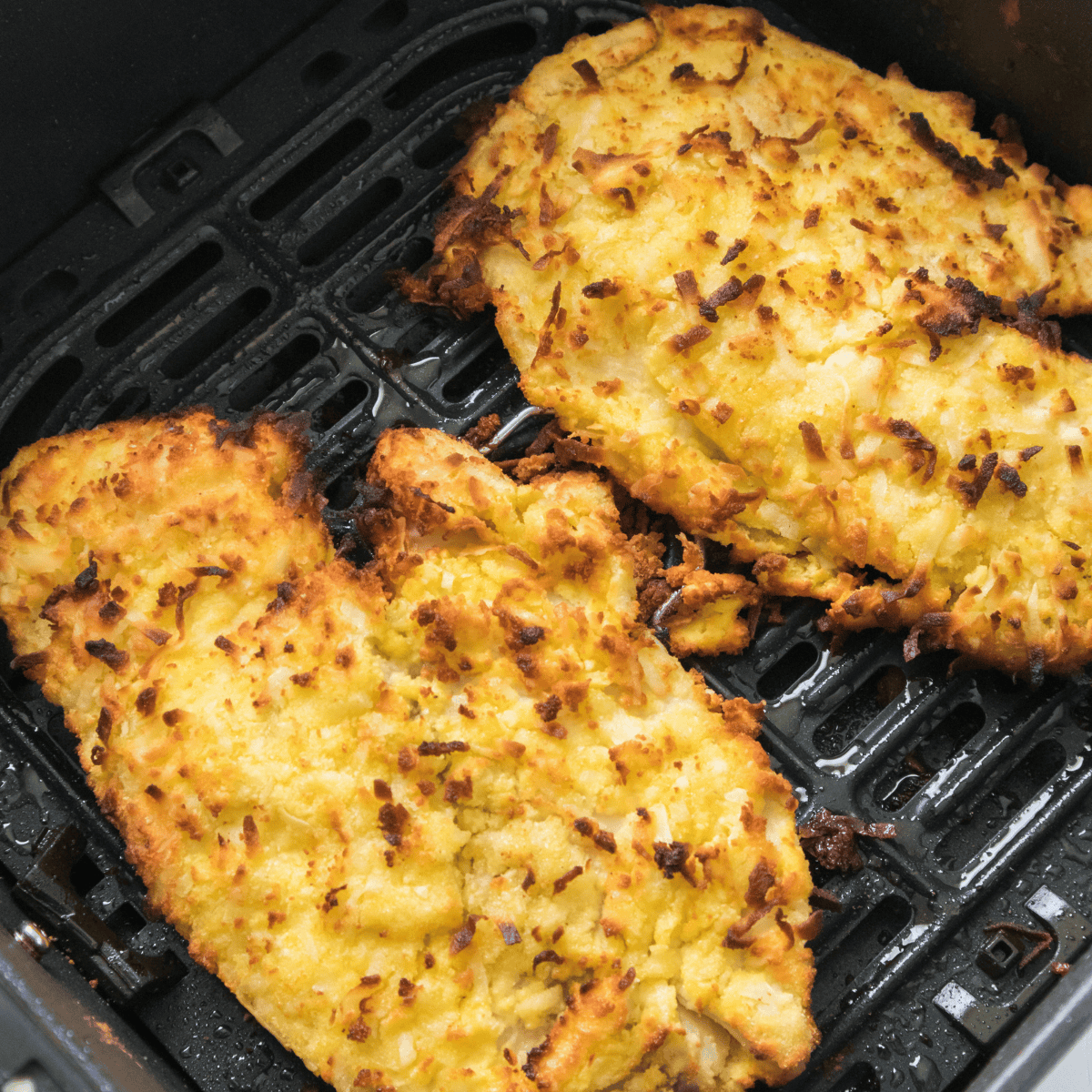 Golden brown air fryer coconut crusted tilapia fillet served on a plate with lemon wedges and herbs