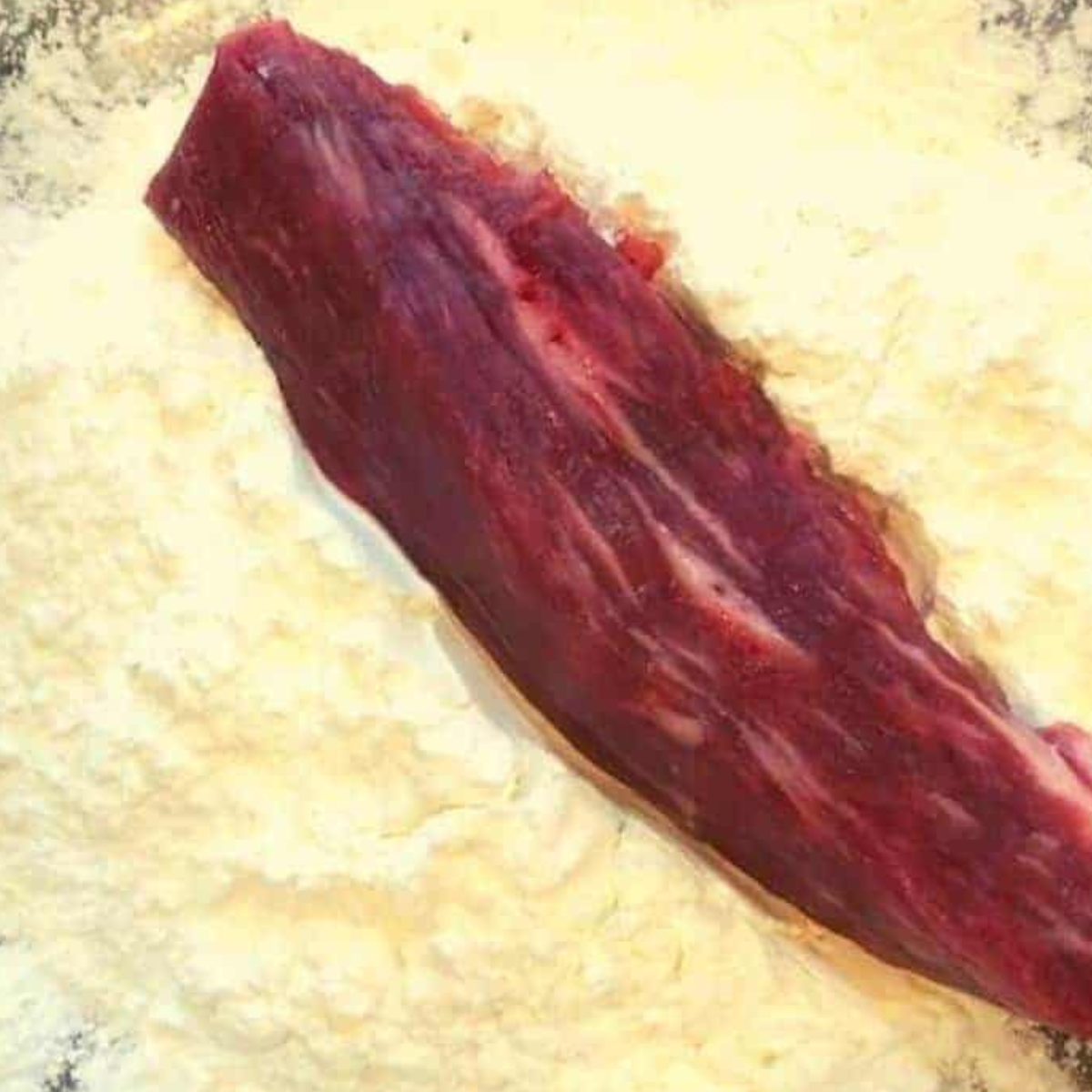 Tossing flank steak in cornstarch. Coating it for crispy texture.