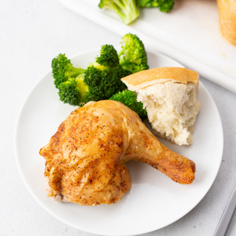Chicken drumsticks served with bread and broccoli on a white plate