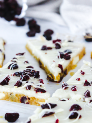 Air fryer cranberry bliss bars cut into triangles, topped with orange cream cheese frosting, dried cranberries, and white chocolate drizzle