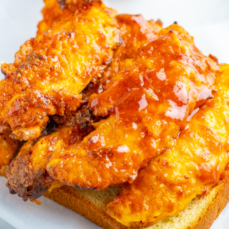 Close-up of golden Nashville hot chicken tender torn open showing juicy interior and craggy spicy crust