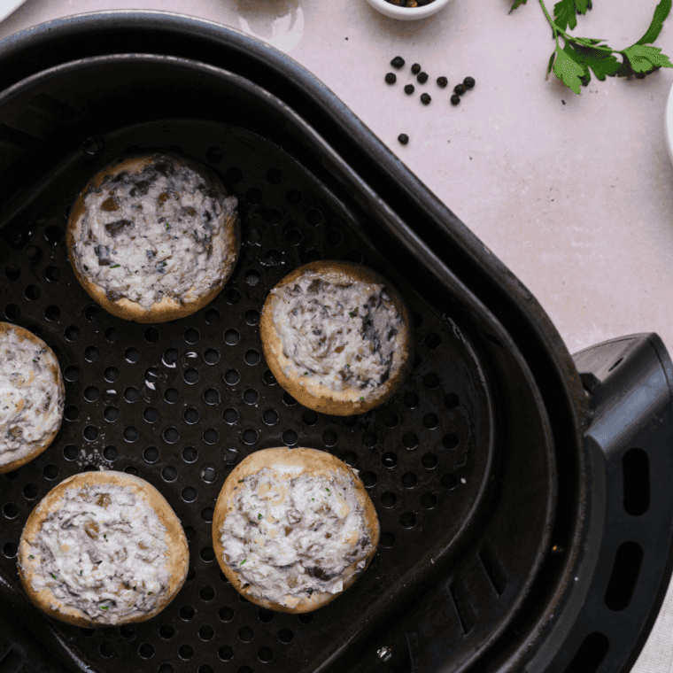 Stuffed mushrooms in air fryer basket, cooked to golden brown, with optional tomato cream sauce drizzle.