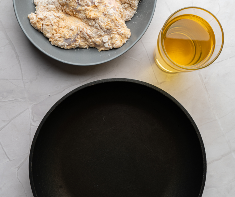 Seasoned flour dredge in a shallow dish beside a wire rack and Dutch oven