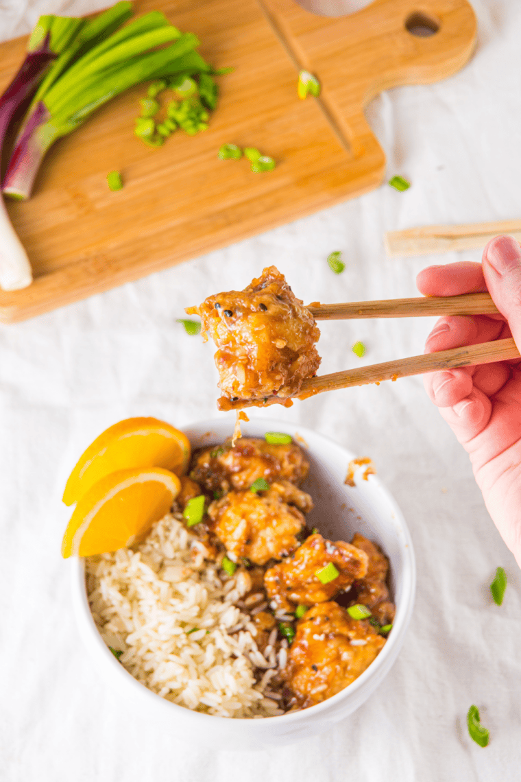 Sticky orange chicken pieces in a slow cooker with sauce being stirred
