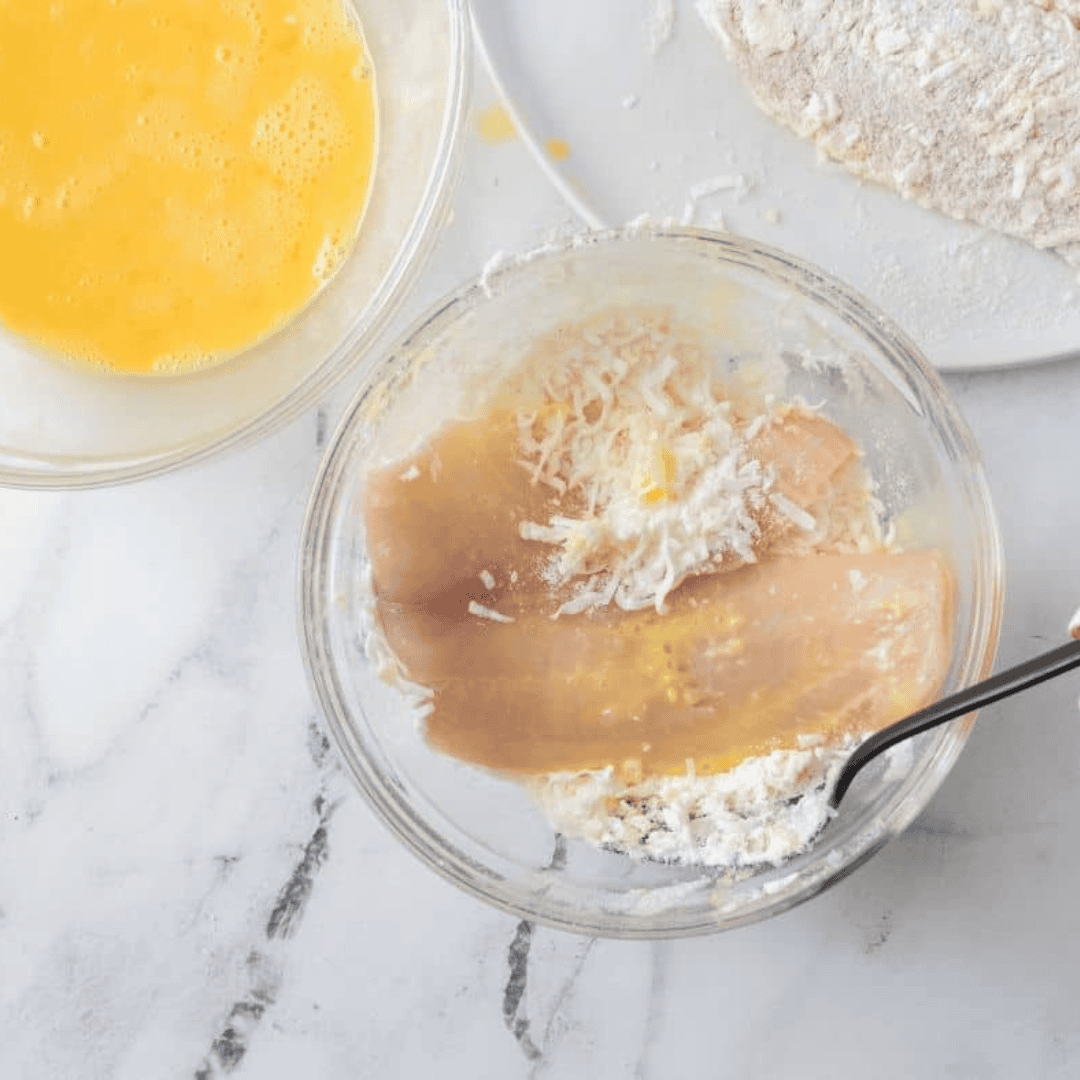  Dipping tilapia fillets into beaten eggs, coating them with the coconut mixture, and preparing to place them in a sprayed air fryer basket