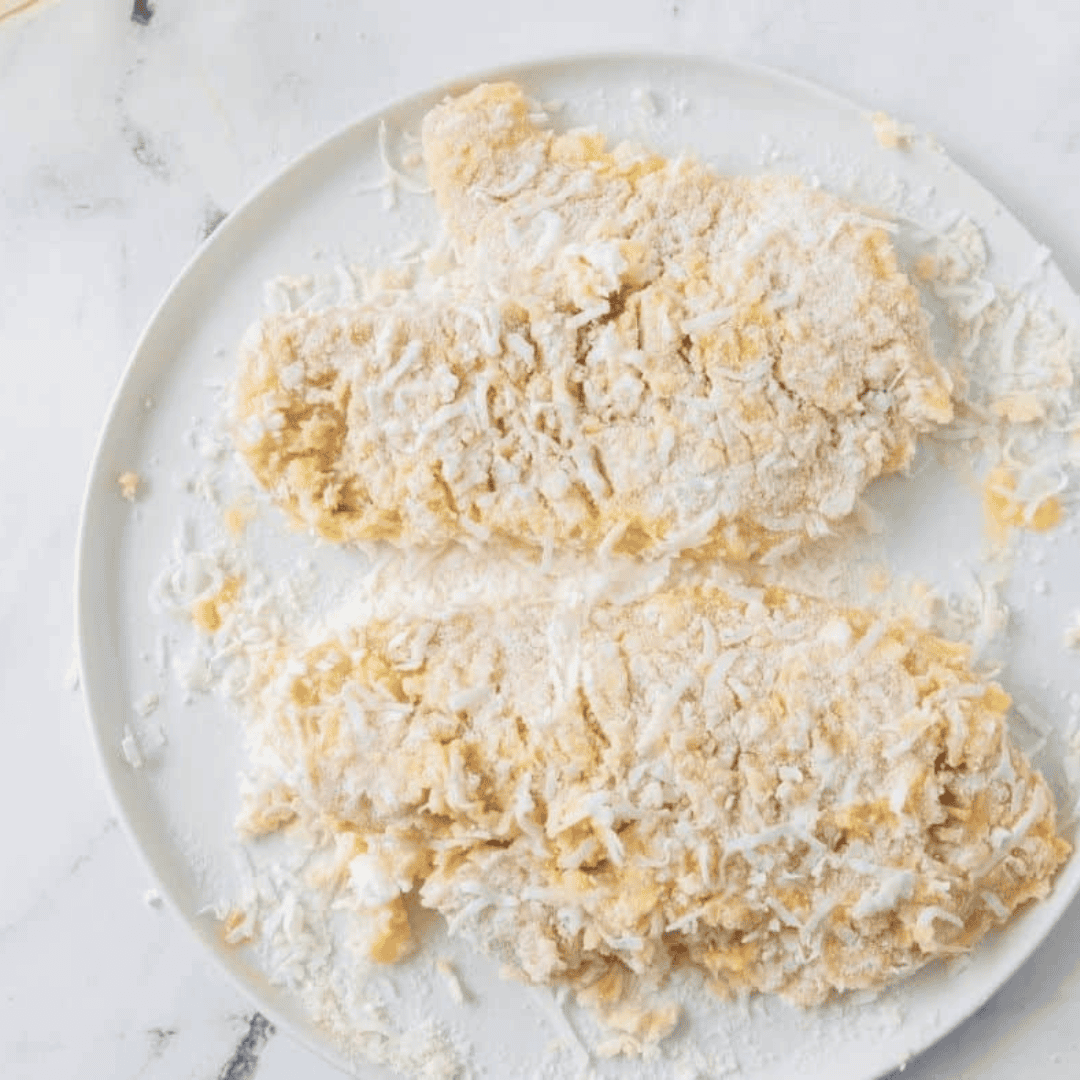 Placing coconut crusted tilapia fillets into the air fryer basket and spraying with olive oil before air frying at 400°F