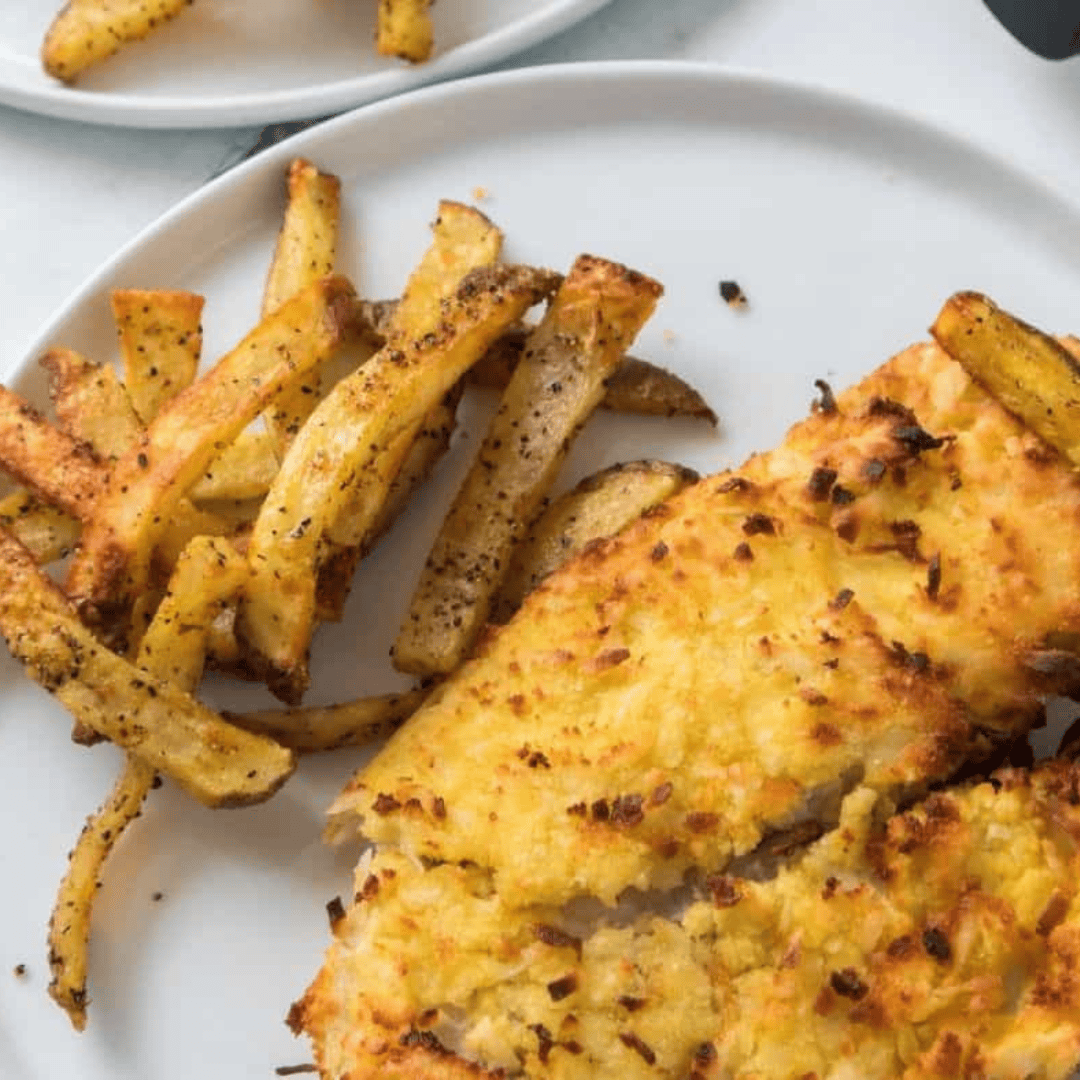 Crispy air fryer coconut crusted tilapia fillet served on a plate with lemon wedges and fresh herbs