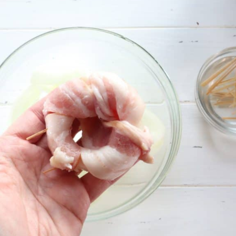 "Bacon wrapped tightly around onion rings, secured with toothpicks, placed in an olive oil-sprayed air fryer basket for cooking."