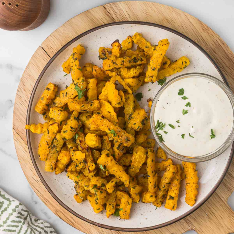 Plate of golden brown Air Fryer Butternut Squash Fries garnished with fresh herbs.