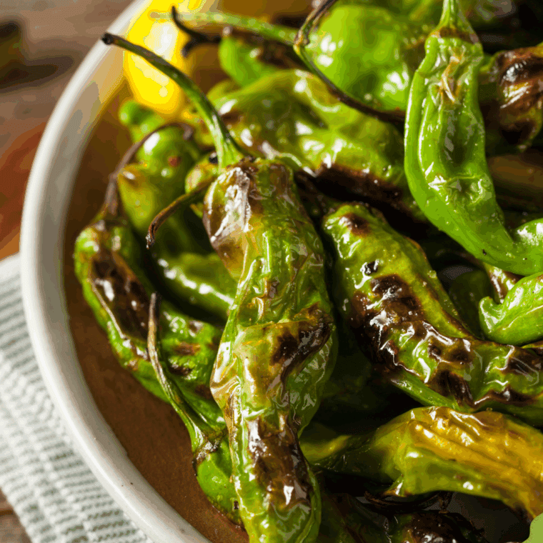 Benihana-style shishito peppers, blistered and seasoned, served on a white plate.