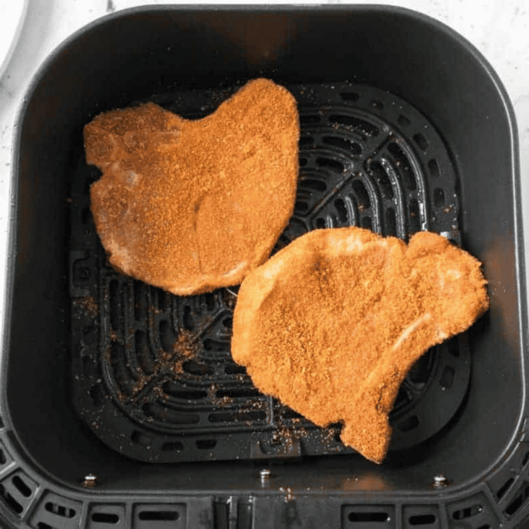 Seasoned bone-in pork chops in a single layer in an air fryer basket