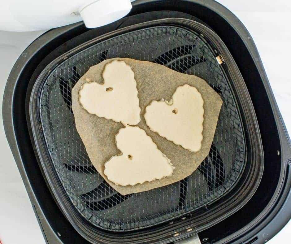 Placing dough ornaments on parchment paper in the air fryer and cooking for 30 minutes until fully dried.