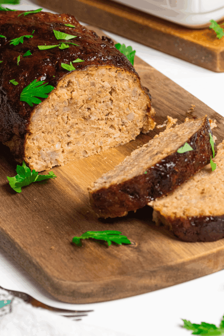 Freshly baked Joanna Gaines meatloaf sliced and served on a plate with herbs.