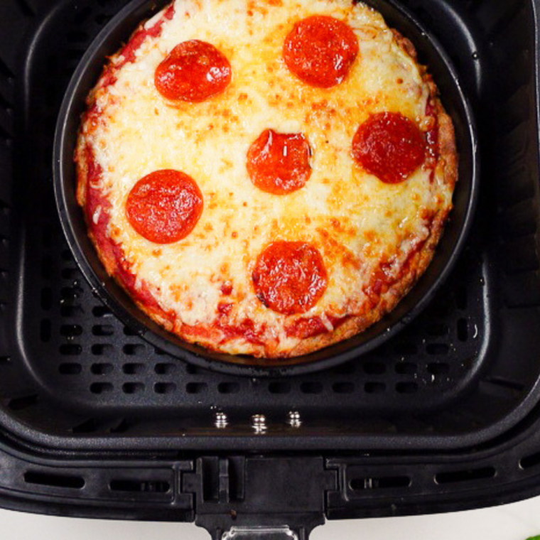 Par-baked pizza crust topped with mozzarella and pepperoni in an air fryer basket, ready for the final cook
