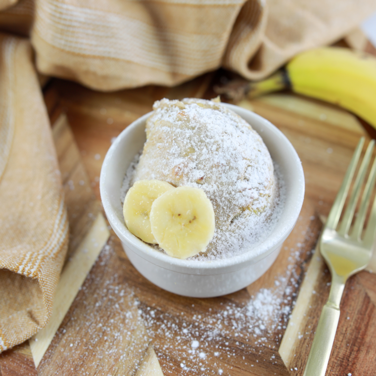 Air fryer banana bread mug cake dusted with powdered sugar, served on a wooden table