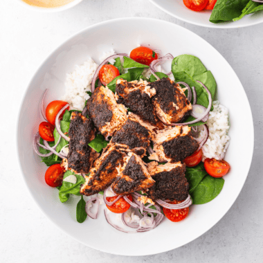 Air fryer blackened salmon fillet with a crispy, dark spice crust, garnished with lemon and fresh herbs on a white plate