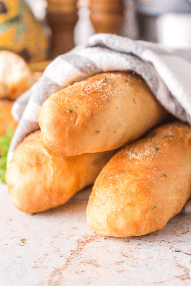 Golden breadsticks on a plate with visible parmesan and herb seasoning