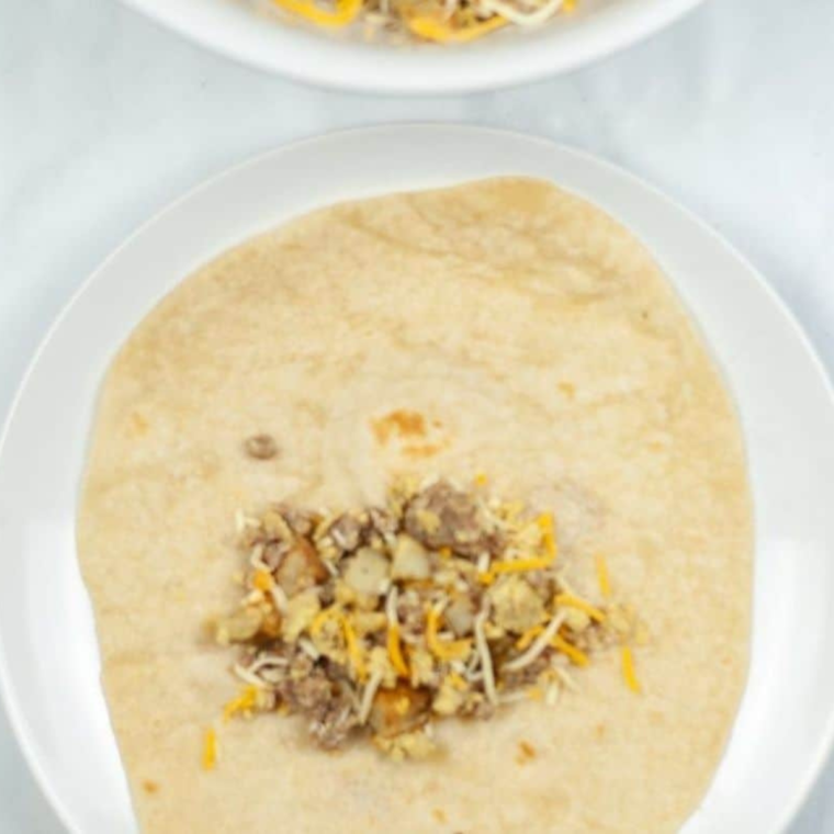 Flour tortilla being filled with the sausage and egg mixture and rolled into a chimichanga