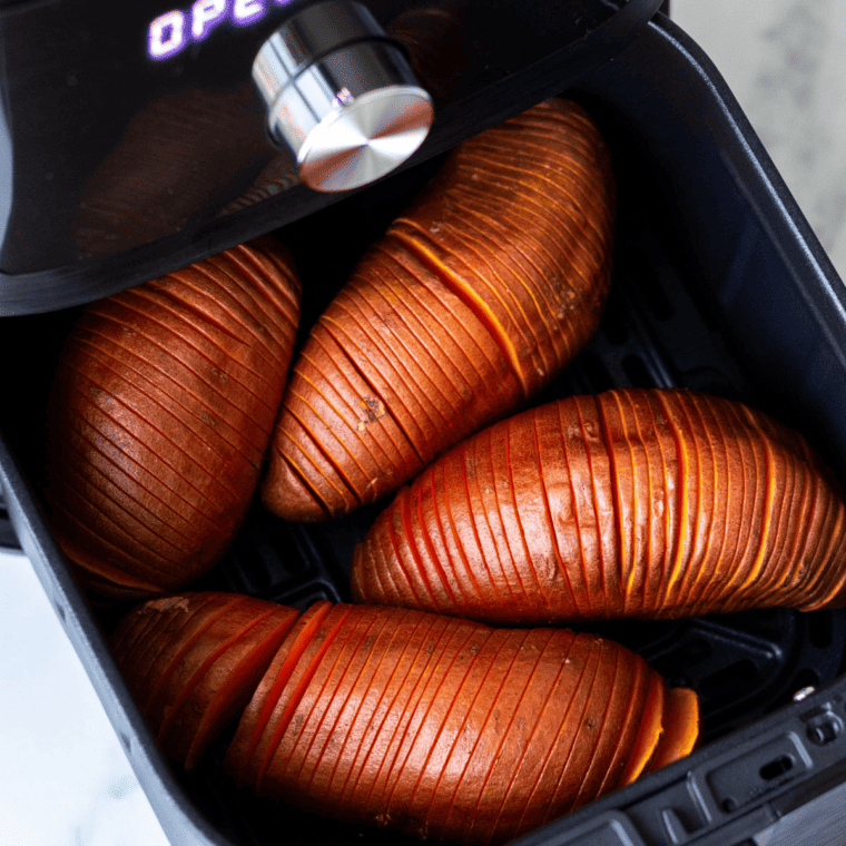 Air fryer basket with arranged hasselback sweet potatoes ready to cook.