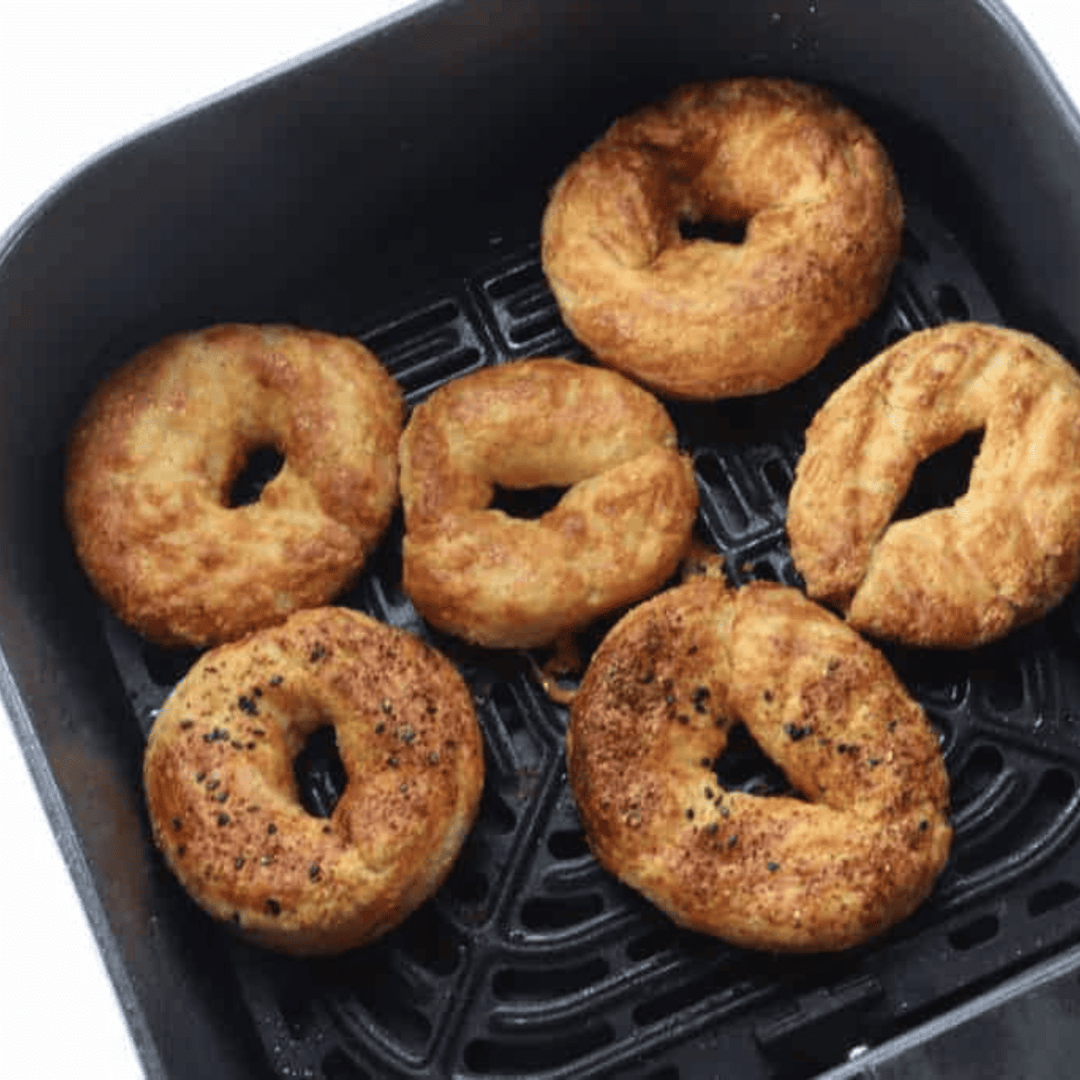 Golden brown keto bagels being flipped with tongs in the air fryer basket halfway through cooking at 350F.