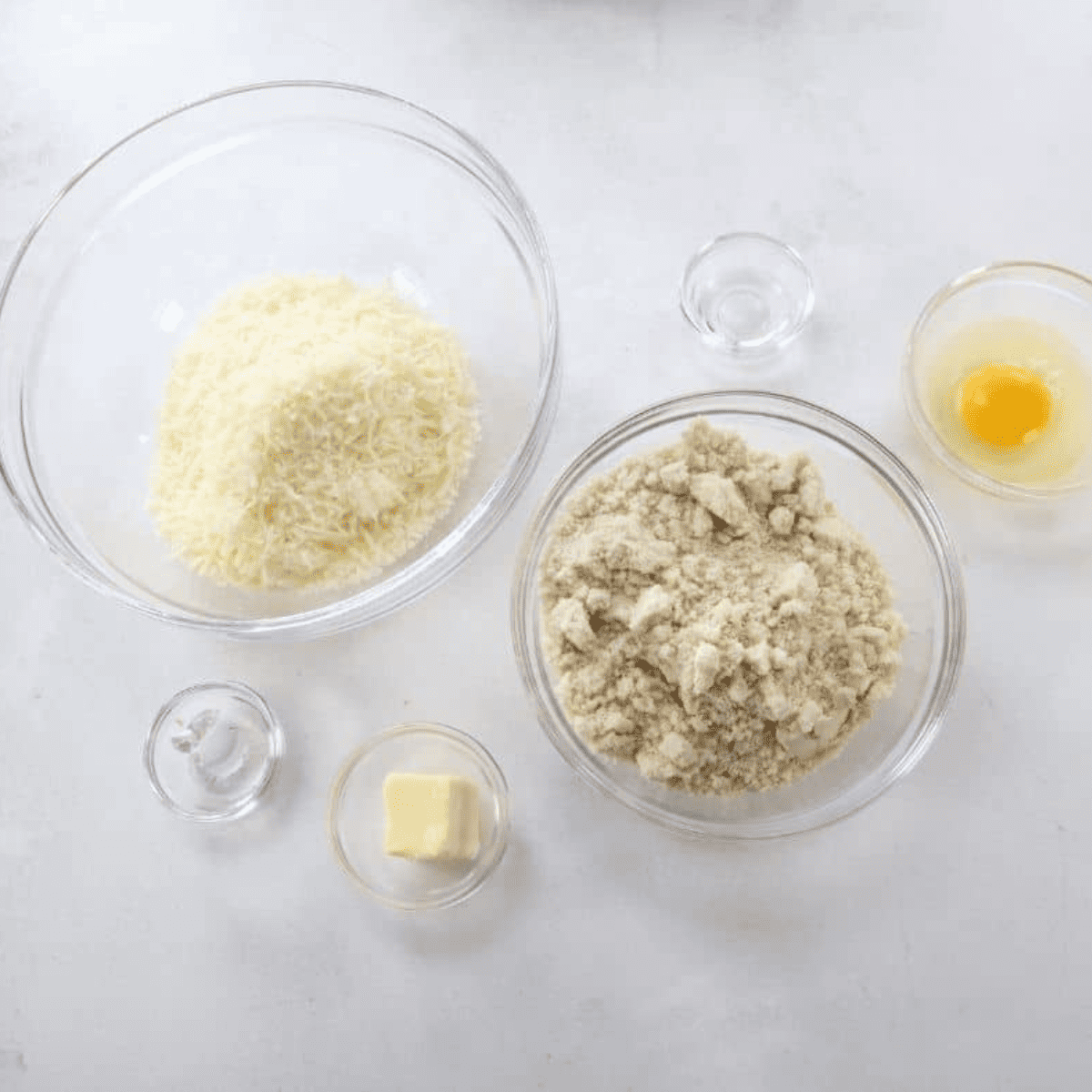 All ingredients needed for air fryer keto bagels measured into bowls β shredded mozzarella, cream cheese, almond flour, baking powder, vinegar, egg, and butter.