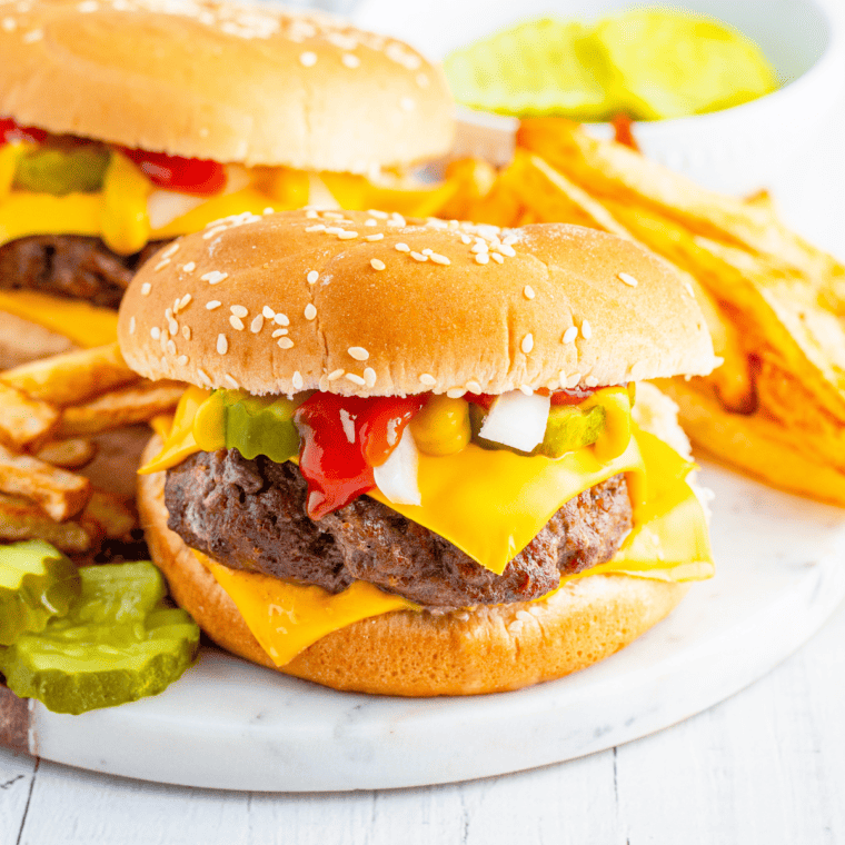 A picture of quarter pounder burgers on plate with pickles on the side.