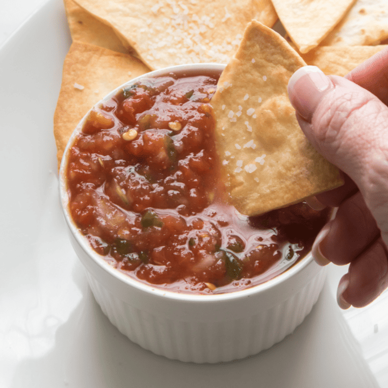 Dipping a tortilla chip into a small bowl of my air fryer roasted salsa recipe