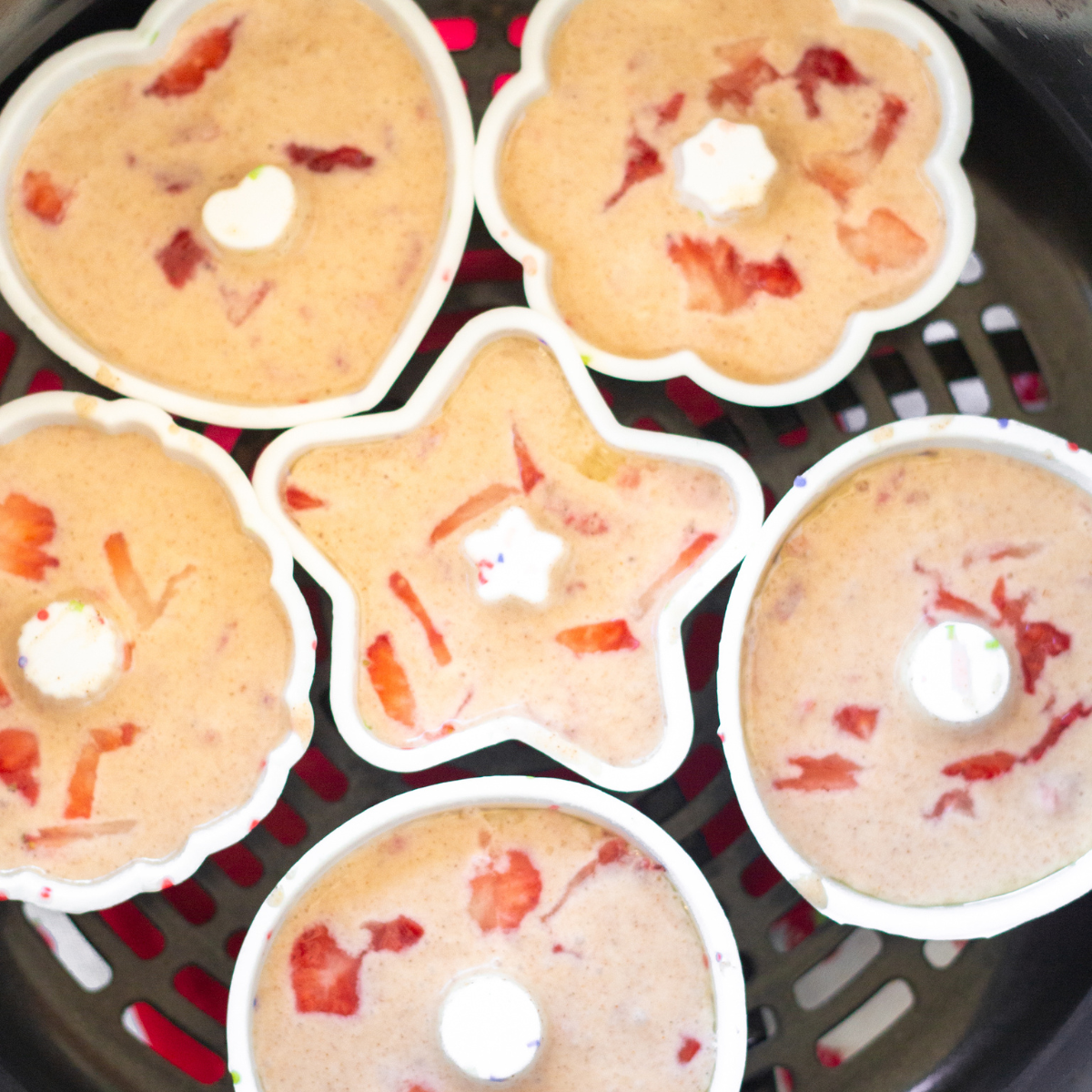 Finished air fryer strawberry donuts being glazed with pink strawberry icing