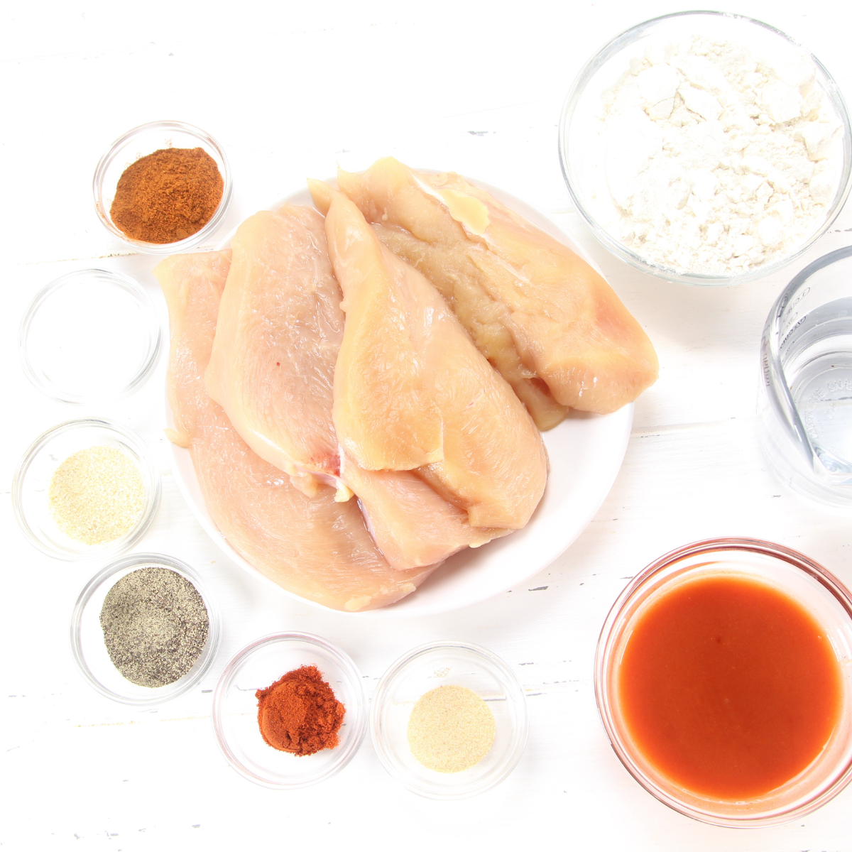 Small bowl with Frank's Red Hot Sauce and water next to a medium bowl filled with a seasoned flour mixture for coating chicken.