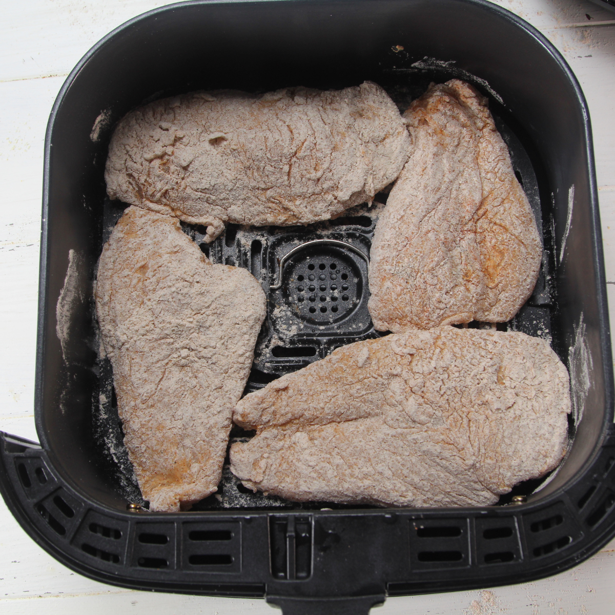 Chicken breasts in an air fryer basket, generously sprayed with cooking spray to ensure a crispy, golden coating while cooking evenly.