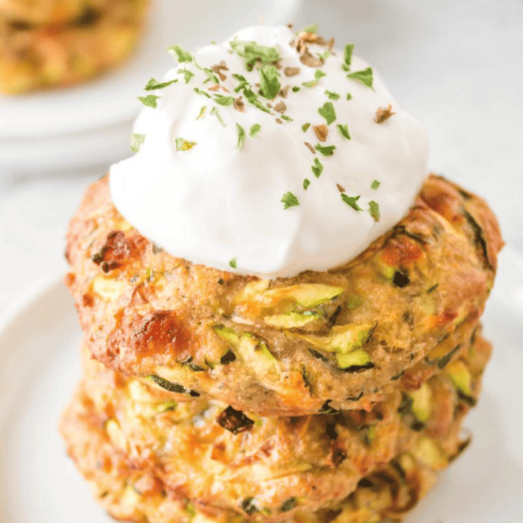 Golden-brown Air Fryer Zucchini Fritters served on a plate, garnished with fresh herbs and a dipping sauce.