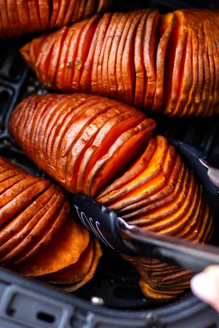 Fork slicing into tender air fryer hasselback sweet potatoes with herbs.
