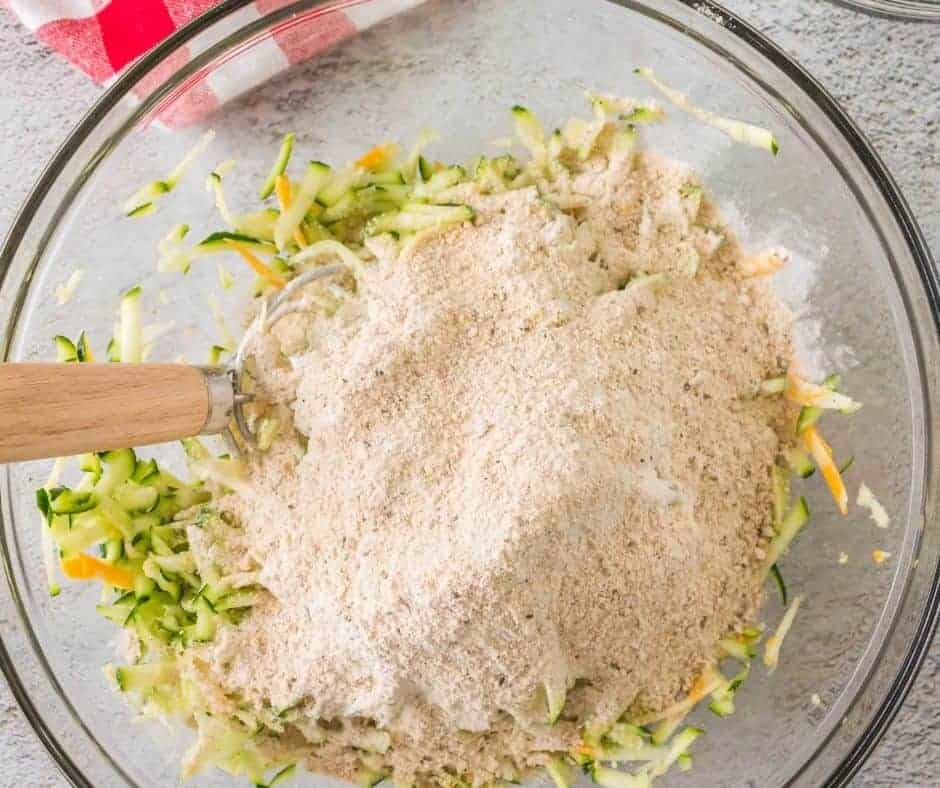 Mixing grated zucchini with eggs, breadcrumbs, and spices in a bowl.