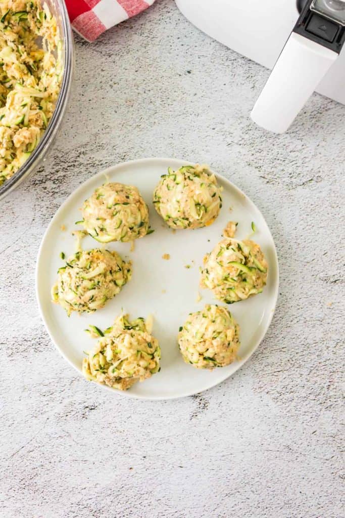 Forming zucchini mixture into small fritters on a parchment-lined tray.