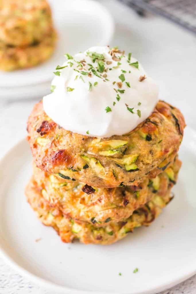 Garnished Air Fryer Zucchini Fritters on a plate with dipping sauce.