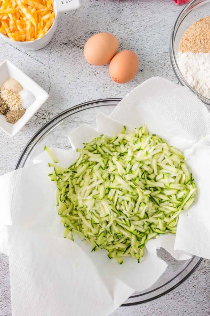 Grated zucchini in a bowl, mixed with salt, sitting to drain excess moisture.