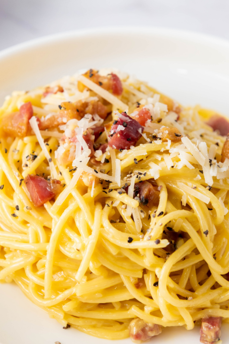 Plate of Slimming World friendly Spaghetti Carbonara with crispy bacon, creamy sauce, and a sprinkle of Parmesan cheese, garnished with fresh parsley.