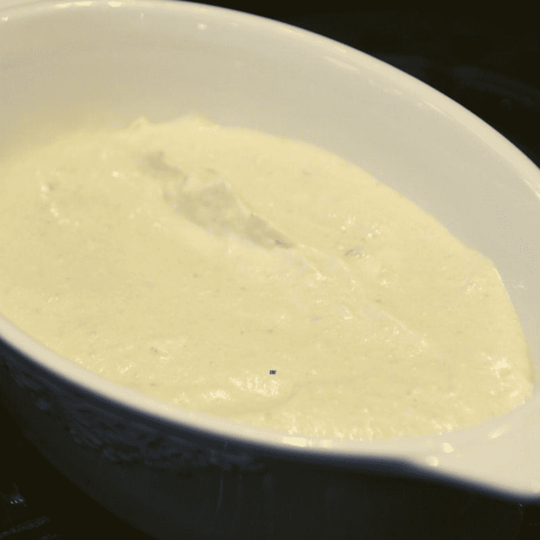 A mixing bowl filled with artichokes, cream cheese, mayonnaise, and seasonings being stirred together.