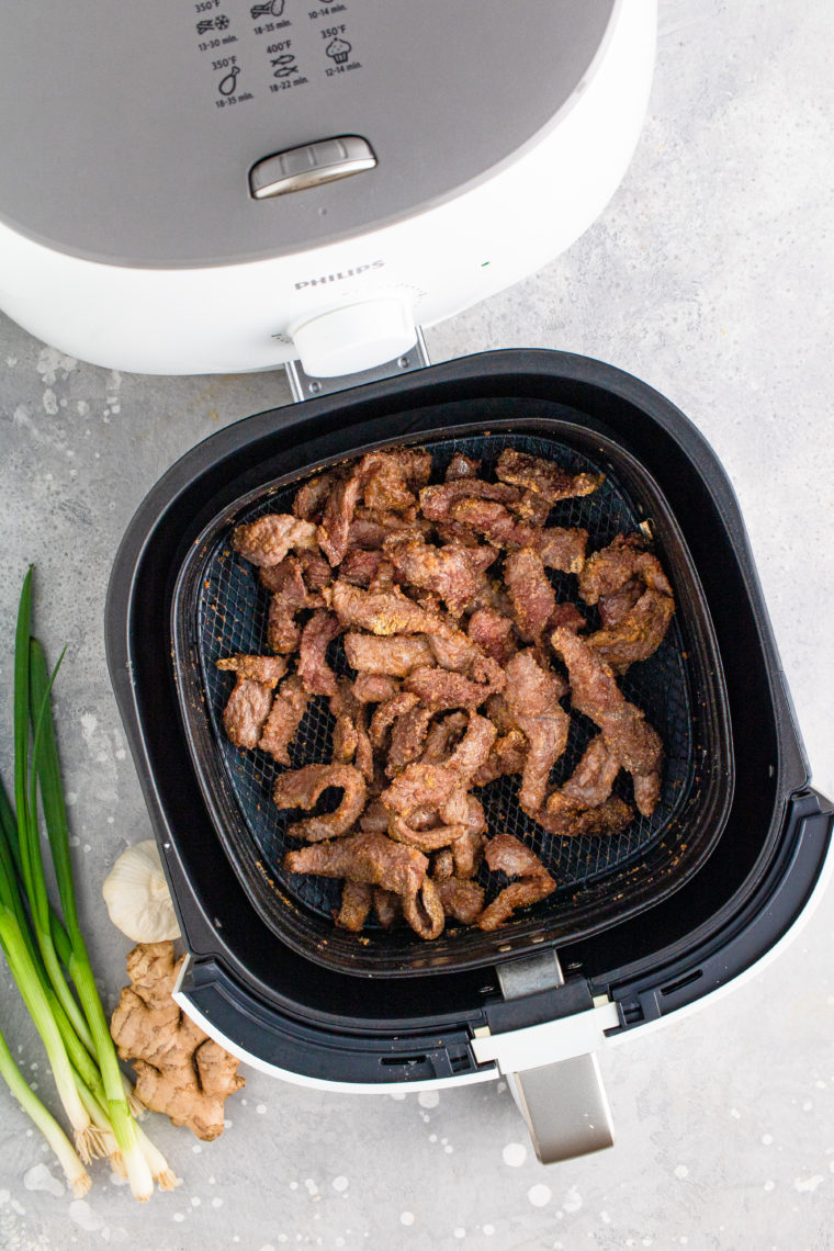 Beef placed in an air fryer basket, sprayed with cooking spray, air frying to crispy perfection while shaking every 5 minutes.
