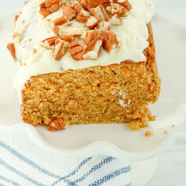 Air fryer carrot cake loaf with a golden-brown crust, topped with cream cheese frosting and garnished with chopped walnuts on a wooden platter.
