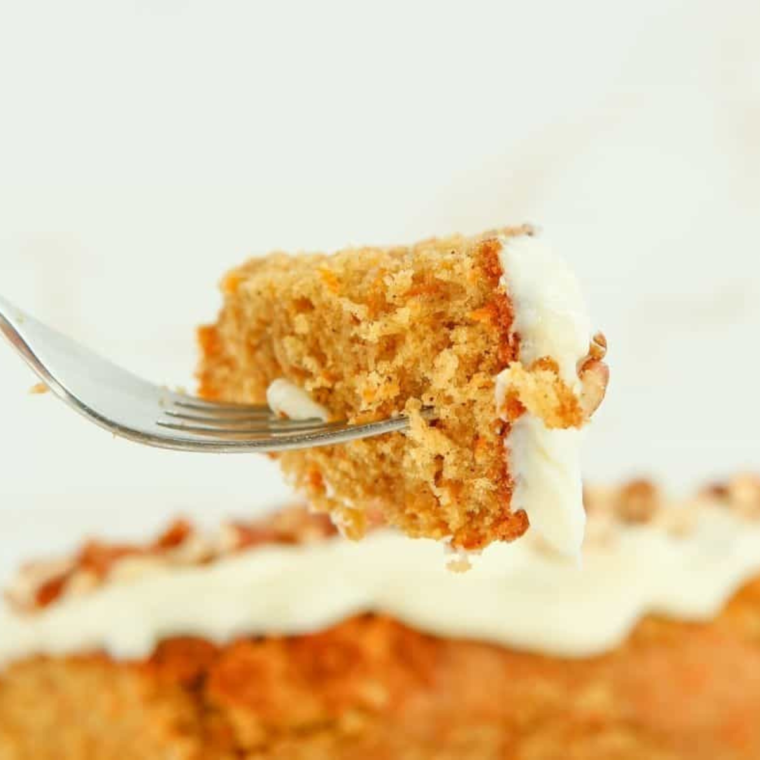 Air Fryer Carrot Cake Loaf on a wooden platter, topped with cream cheese frosting and garnished with chopped walnuts, ready to be served.